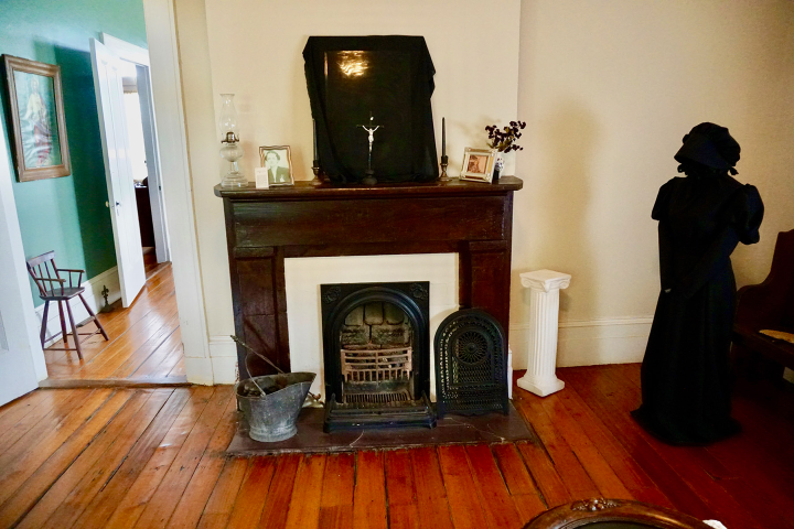Room with a fireplace, dark cloth, framed photos, and a black-clad mannequin.