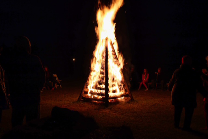 Large bonfire at night surrounded by people.