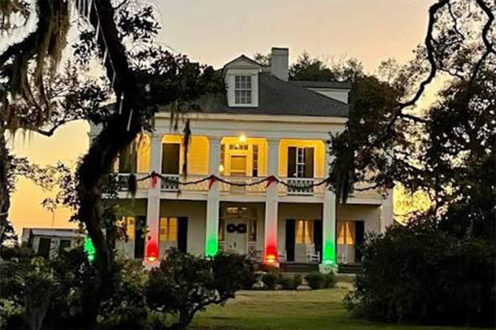 Large two-story house with colored lights and porch columns at dusk.