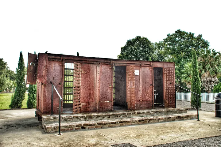 Rusty old jail cell structure outdoors with trees in the background.