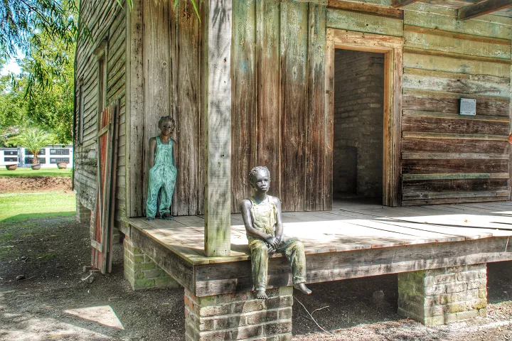 Two bronze sculptures of children sitting on a wooden cabin porch.