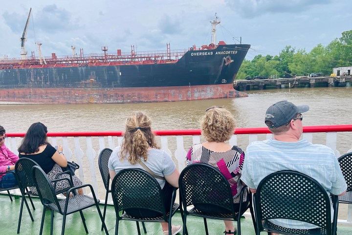 People sitting on a boat viewing a large cargo ship passing by on a river.
