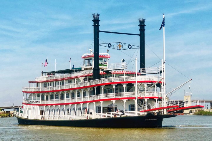 Paddle steamboat with red and white trim on a river under a blue sky.