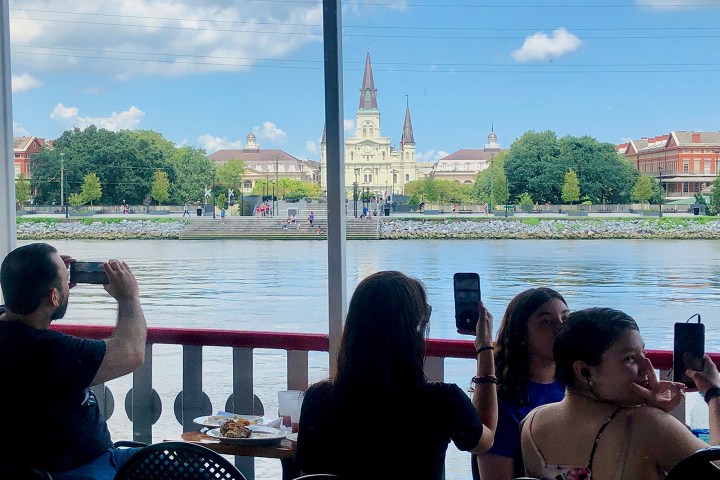People on a boat taking photos of a riverside cityscape with a cathedral in the background.