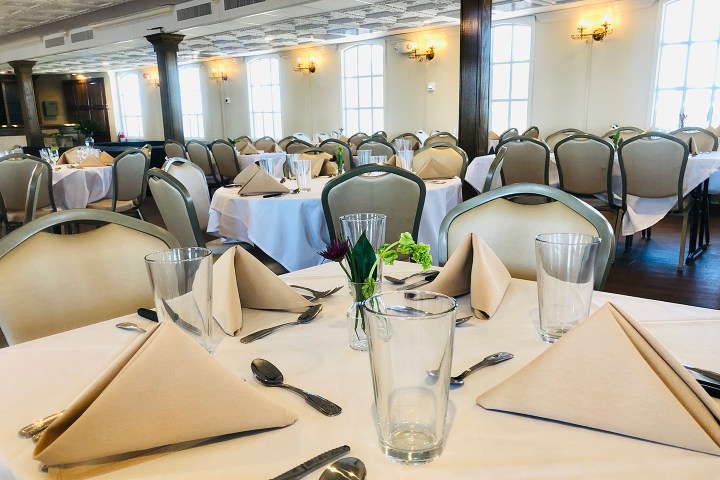 Elegant dining room with round tables, white tablecloths, and beige napkins folded into triangles.