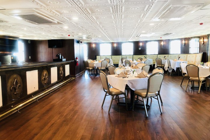 Elegant dining room with round tables, white tablecloths, and beige chairs on wooden floor.