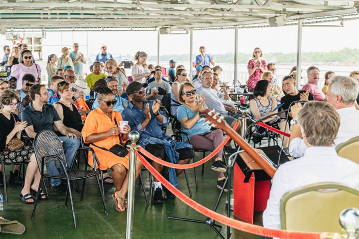 People seated on a boat, clapping and watching a musical performance.