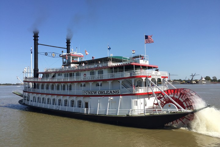 Paddle steamboat 'New Orleans' on water, with flags and city skyline in background.