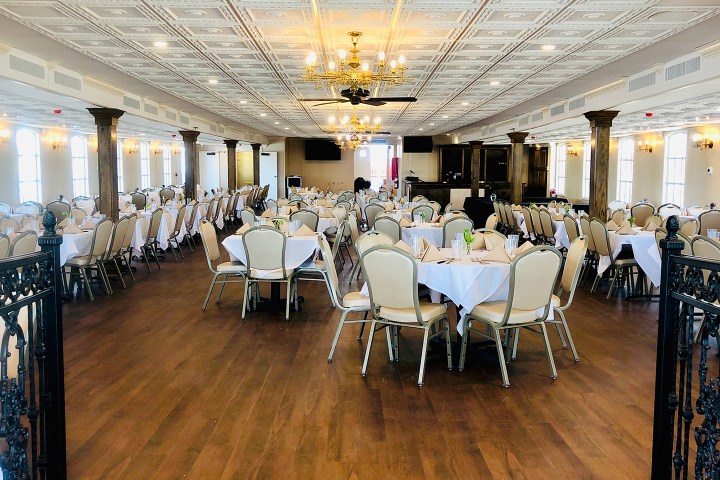 Elegant banquet hall with round tables, white tablecloths, chandeliers, and wooden flooring.