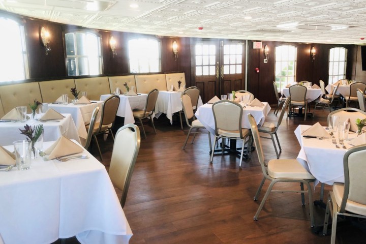 Elegant dining room with tables set for guests, featuring white tablecloths and padded chairs.