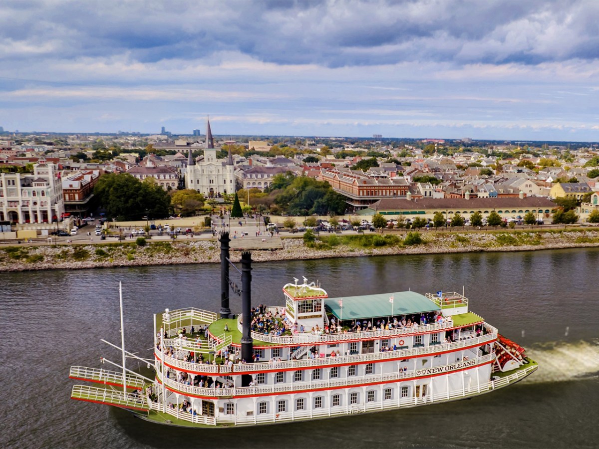 Paddle steamboat on river with cityscape and cloudy sky background.