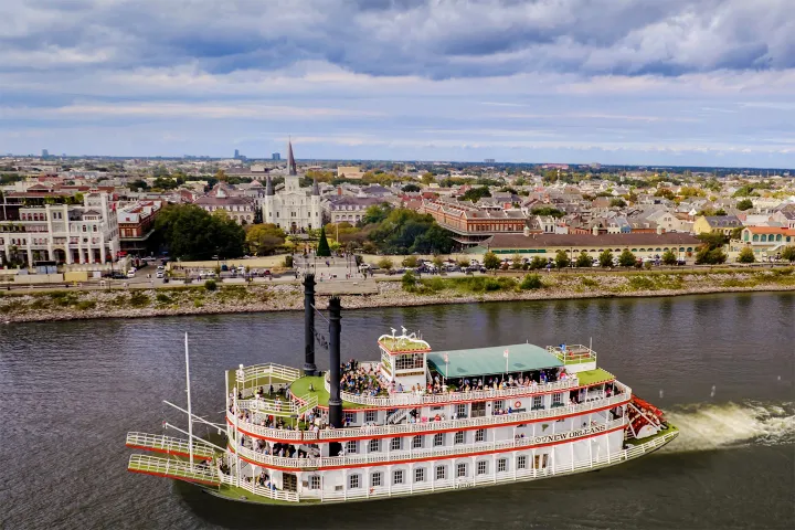 Paddle steamboat on river with cityscape and cloudy sky background.