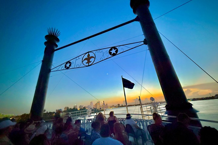 People on a boat at sunset with city skyline and a decorative arch above.