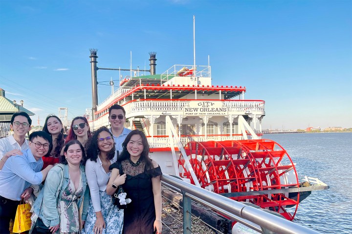 Group of people posing in front of a riverboat labeled 'City of New Orleans' by the water.