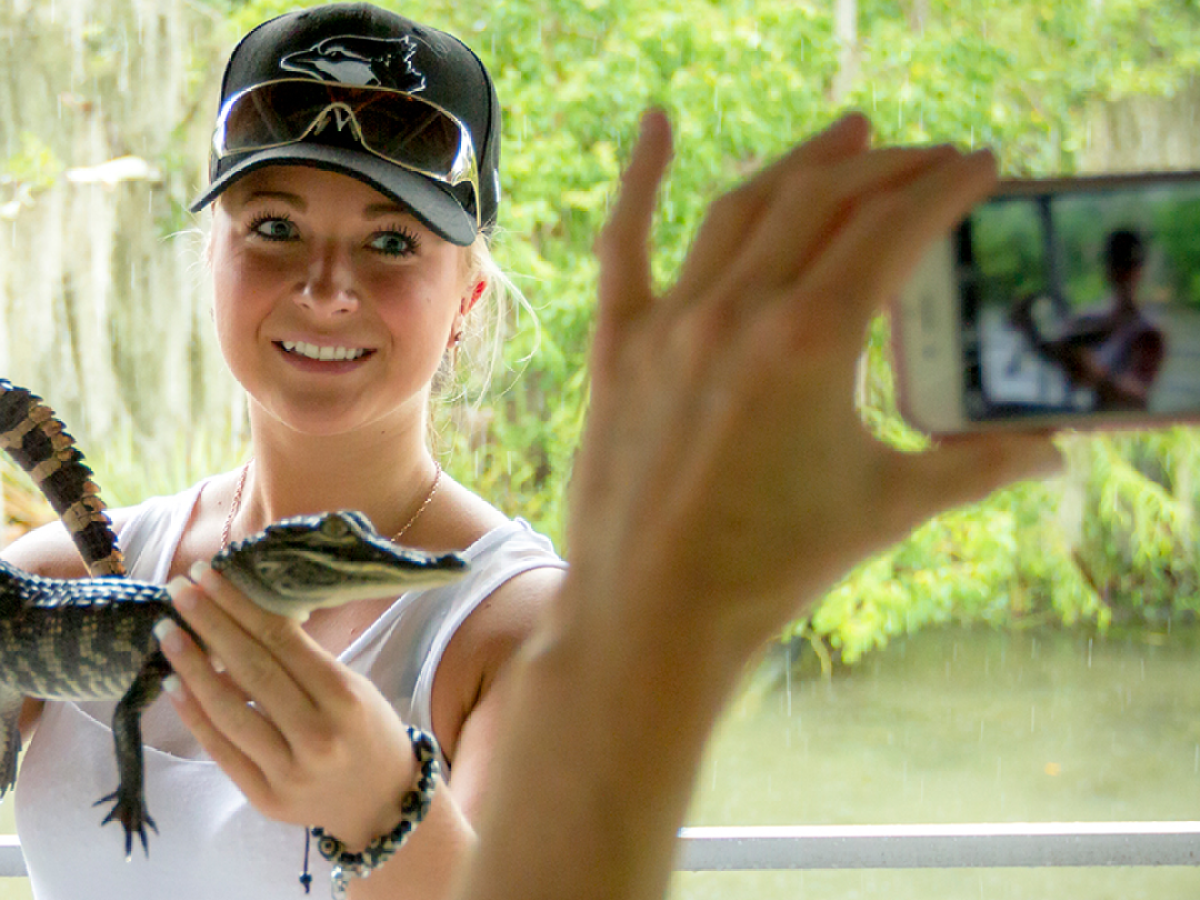 Person holding small alligator while another takes a photo.