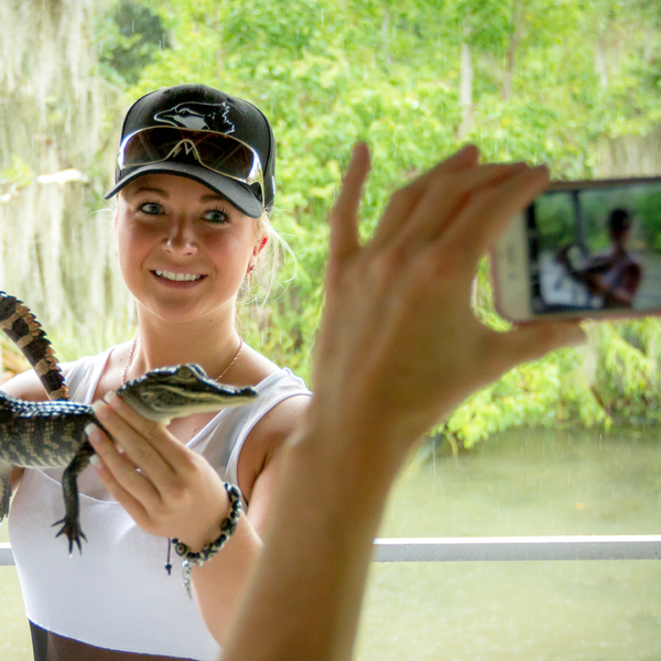 Person holding small alligator while another takes a photo.