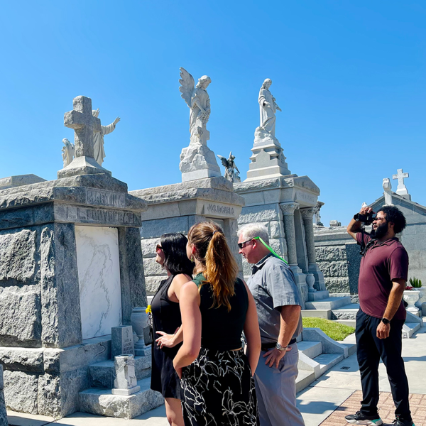 Group of people walking through a historic cemetery with ornate mausoleums on a sunny day.