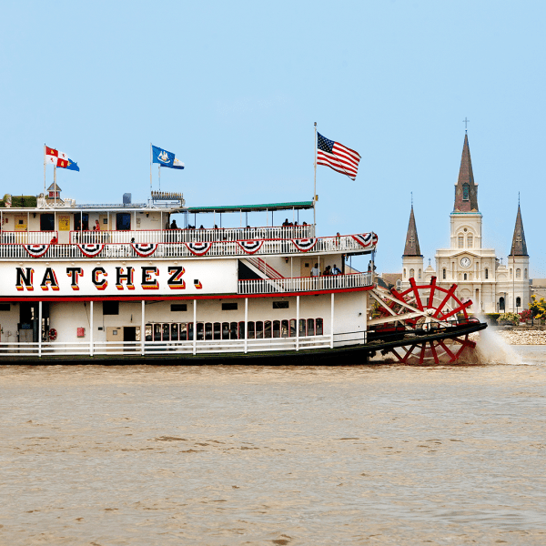 Steamboat on river with flags, cityscape and church steeple in background.