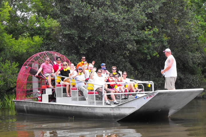 Group of people on an airboat in a river with lush greenery.