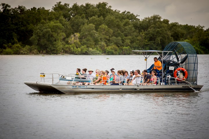 Tourists on an airboat ride through a lake with surrounding trees.