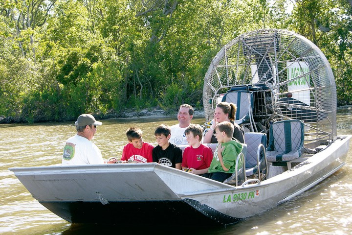 Group of people sitting in an airboat surrounded by trees and water.