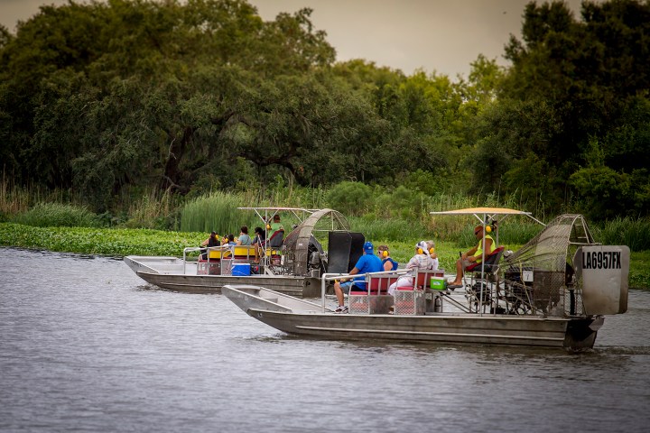 Two airboats with passengers on a lake near trees and greenery.